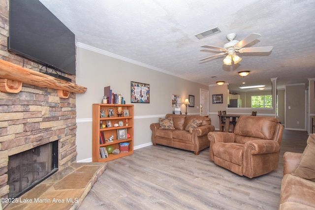 living area with a ceiling fan, a textured ceiling, crown molding, a fireplace, and wood finished floors