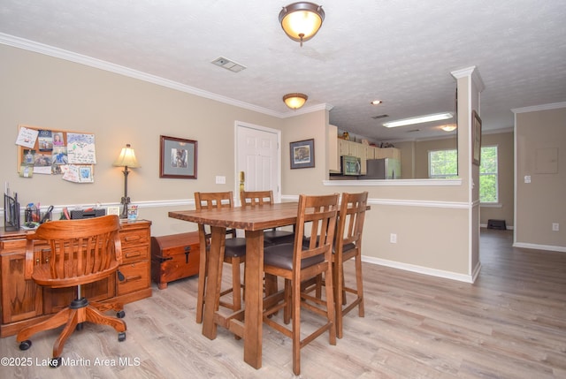 dining area with crown molding, a textured ceiling, light wood-style flooring, baseboards, and visible vents