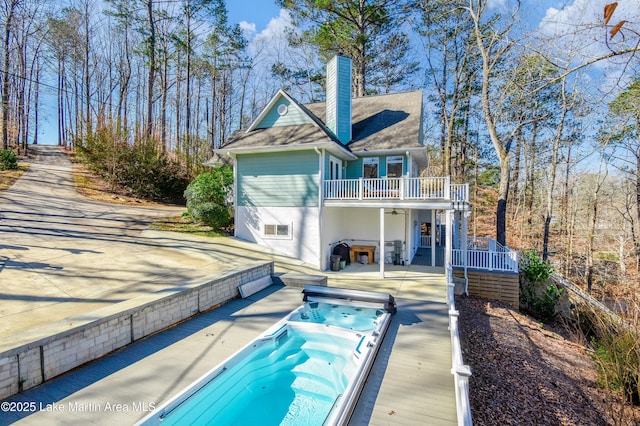 rear view of house with a balcony, hot tub deck surround, and a chimney