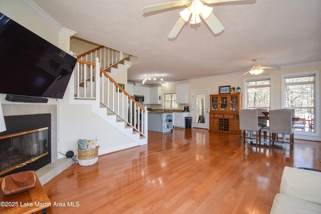 living area with light wood-type flooring, a ceiling fan, ornamental molding, and stairs