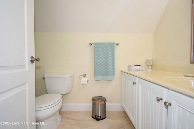 bathroom featuring baseboards, lofted ceiling, toilet, and vanity