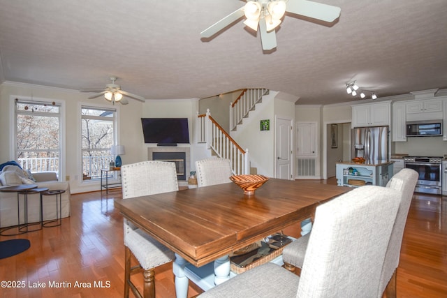 dining area featuring ornamental molding, a tiled fireplace, a ceiling fan, light wood finished floors, and stairs