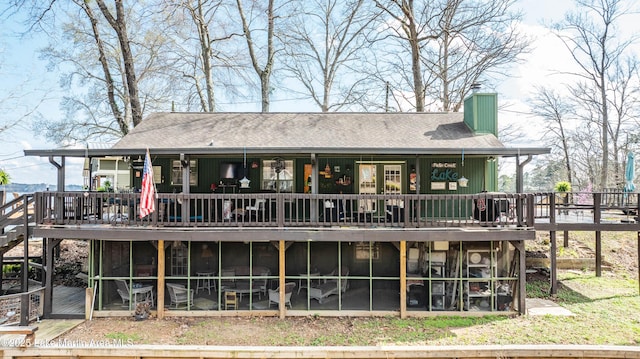 back of property with a wooden deck, roof with shingles, a sunroom, and a chimney