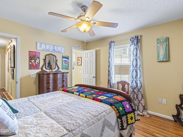 bedroom with a ceiling fan, baseboards, light wood finished floors, and a textured ceiling