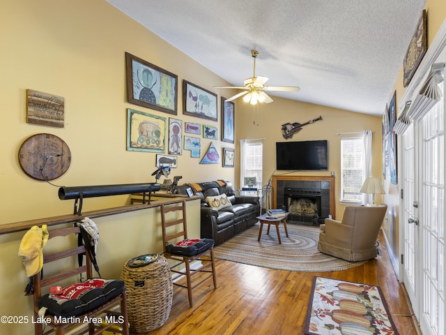 living room with wood finished floors, lofted ceiling, a fireplace, ceiling fan, and a textured ceiling