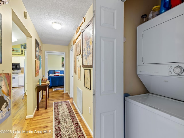 laundry area with visible vents, stacked washer and dryer, a textured ceiling, light wood finished floors, and laundry area