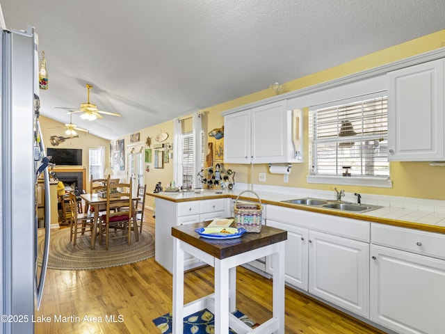 kitchen with a ceiling fan, a sink, white cabinetry, light wood-style floors, and a fireplace