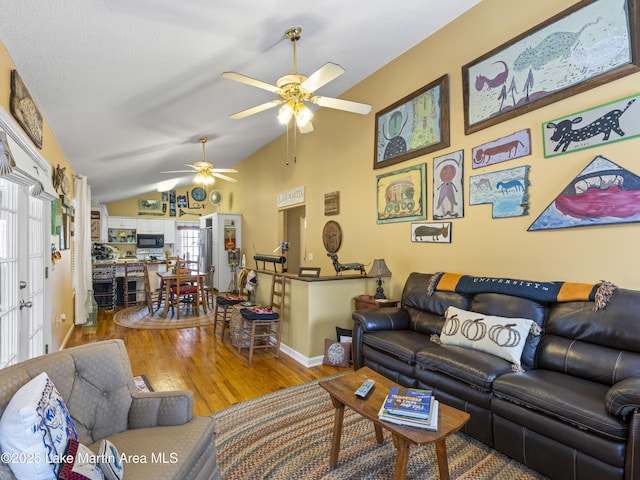 living area featuring vaulted ceiling, baseboards, ceiling fan, and wood finished floors