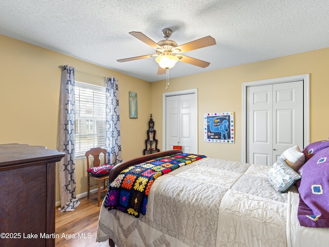 bedroom featuring wood finished floors, baseboards, ceiling fan, multiple closets, and a textured ceiling