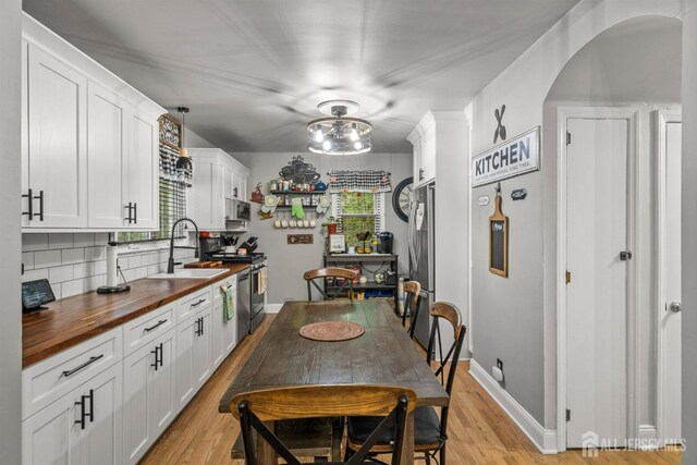 kitchen with wood counters, a sink, stainless steel range with electric stovetop, arched walkways, and backsplash