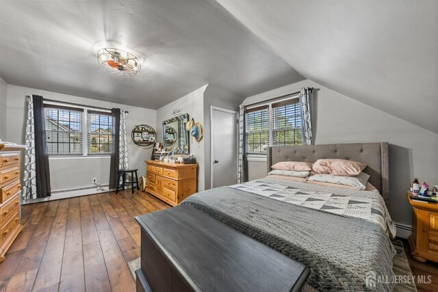bedroom featuring lofted ceiling, multiple windows, dark wood-style floors, a baseboard radiator, and baseboards