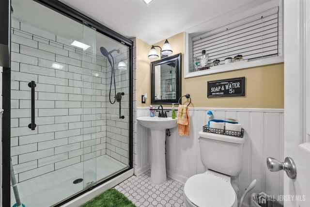 bathroom with toilet, a shower stall, wainscoting, tile patterned flooring, and a sink