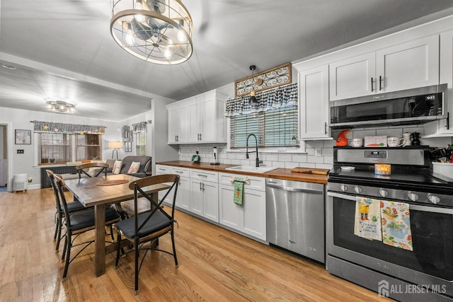 kitchen with appliances with stainless steel finishes, a sink, butcher block counters, light wood-type flooring, and decorative backsplash