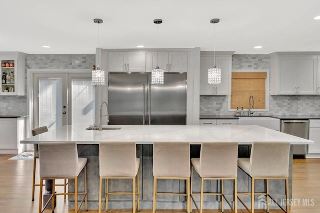 kitchen featuring sink, appliances with stainless steel finishes, a spacious island, light stone counters, and decorative light fixtures