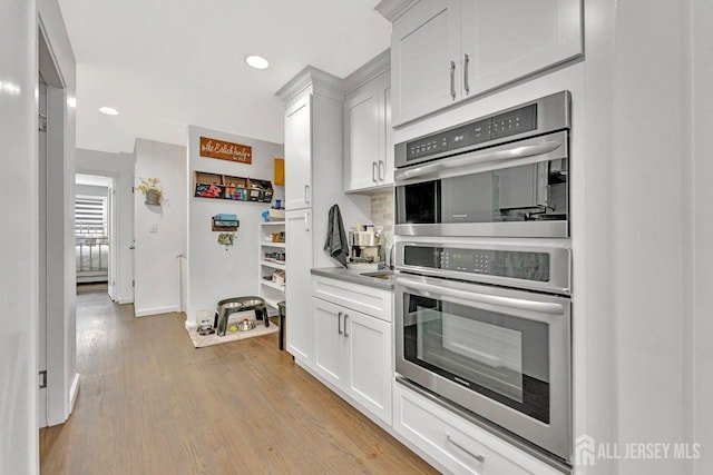 kitchen featuring stainless steel double oven, light hardwood / wood-style flooring, and white cabinets