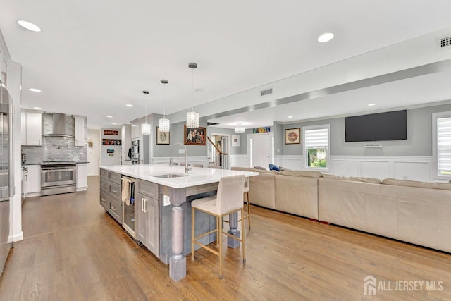 kitchen featuring an island with sink, sink, white cabinets, hanging light fixtures, and stainless steel range oven