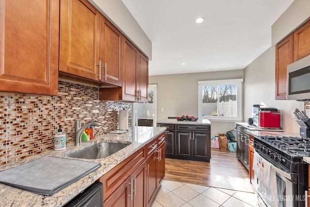 kitchen with sink, backsplash, light tile patterned floors, light stone countertops, and gas range oven