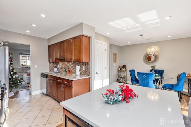 kitchen featuring light tile patterned flooring, light countertops, stainless steel dishwasher, brown cabinetry, and pendant lighting