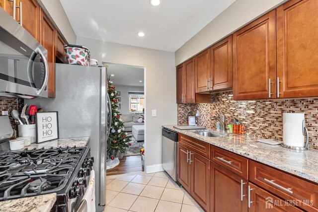 kitchen with sink, backsplash, stainless steel appliances, light stone counters, and light tile patterned flooring