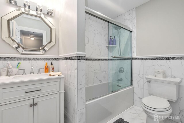 bathroom featuring enclosed tub / shower combo, marble finish floor, wainscoting, and toilet