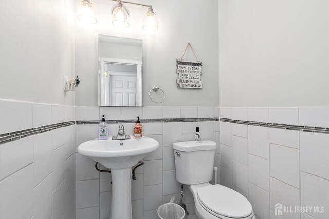 half bath with a wainscoted wall, toilet, and tile walls