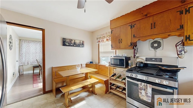 kitchen with ceiling fan, brown cabinetry, stainless steel range with gas stovetop, and baseboards