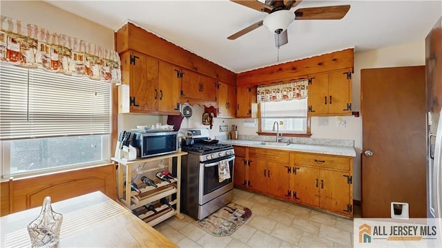 kitchen featuring stainless steel appliances, a sink, a ceiling fan, light countertops, and brown cabinets