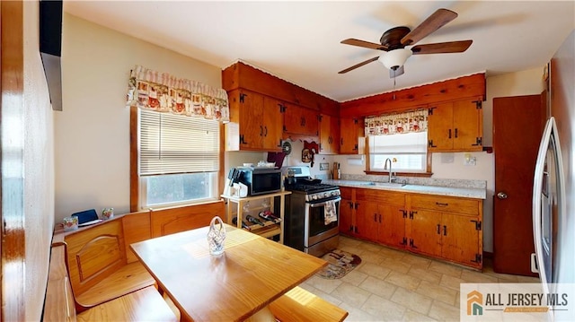 kitchen featuring a sink, a ceiling fan, light countertops, stainless steel gas range, and brown cabinets