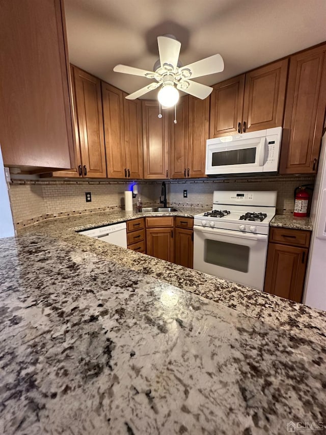 kitchen with sink, tasteful backsplash, ceiling fan, white appliances, and light stone countertops