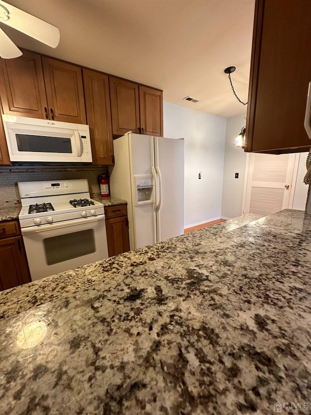 kitchen with white appliances, decorative light fixtures, ceiling fan, light stone countertops, and backsplash