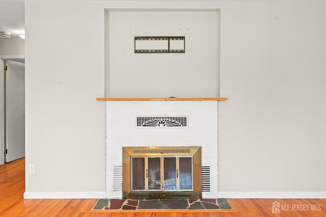 details featuring baseboards, a brick fireplace, wood finished floors, and visible vents