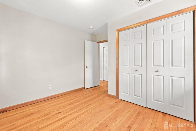 unfurnished bedroom featuring visible vents, light wood-style floors, baseboards, and a closet