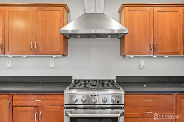 kitchen with dark countertops, high end range, brown cabinets, and wall chimney range hood