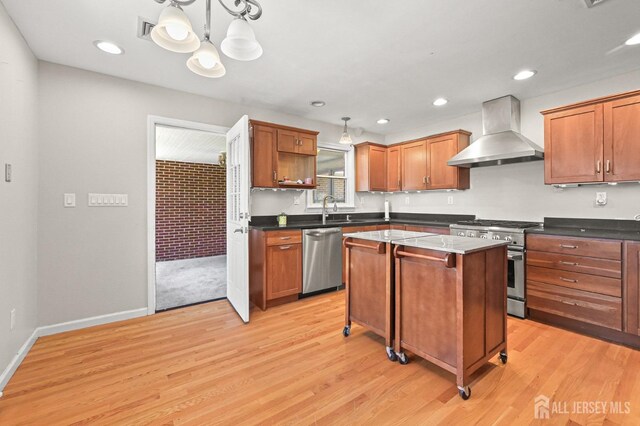 kitchen featuring wall chimney range hood, a kitchen island, appliances with stainless steel finishes, light wood-type flooring, and a notable chandelier