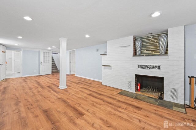 finished basement featuring visible vents, a brick fireplace, stairs, baseboards, and recessed lighting