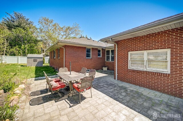 view of patio featuring fence, a storage unit, an outbuilding, and outdoor dining area