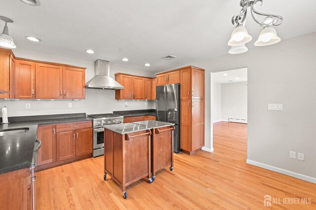 kitchen with light wood-style flooring, wall chimney exhaust hood, appliances with stainless steel finishes, and a baseboard heating unit