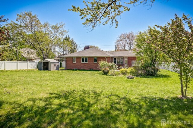 rear view of property featuring a storage shed, an outbuilding, brick siding, fence, and a yard
