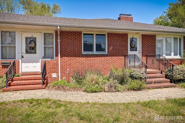 single story home featuring brick siding, a chimney, a shingled roof, and entry steps