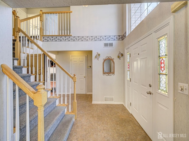 foyer entrance with a towering ceiling, stairway, and baseboards