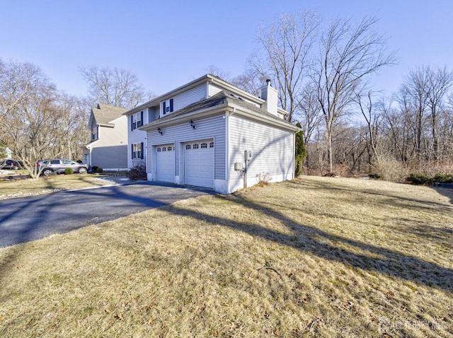 view of side of home featuring asphalt driveway, a chimney, a garage, and a yard