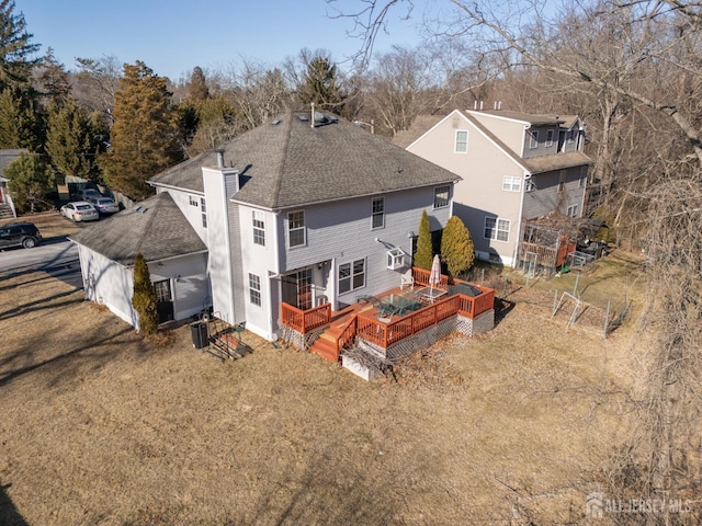 back of house featuring a chimney, a deck, a shingled roof, and fence
