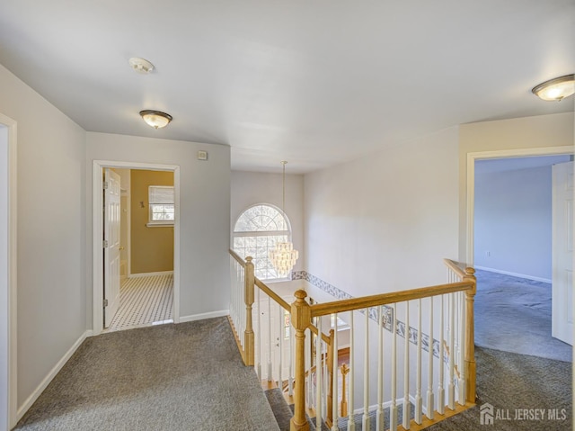 corridor with an upstairs landing, carpet, baseboards, and a chandelier