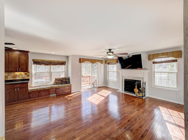 unfurnished living room with ceiling fan, hardwood / wood-style flooring, a fireplace, and baseboards