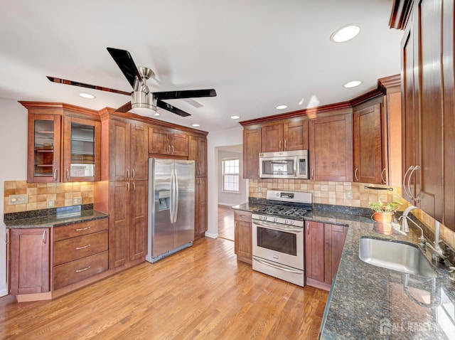 kitchen featuring appliances with stainless steel finishes, a sink, tasteful backsplash, light wood-type flooring, and glass insert cabinets