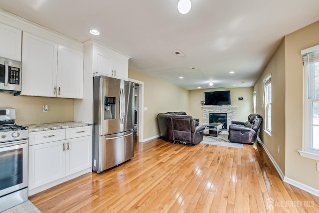 169 Metuchen Ave, Woodbridge Proper, NJ 07095 - kitchen with stainless steel appliances, white cabinetry, light wood-type flooring, a stone fireplace, and light stone countertops