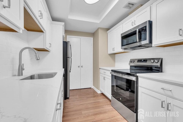 kitchen featuring white cabinets, a raised ceiling, stainless steel appliances, light wood-type flooring, and a sink