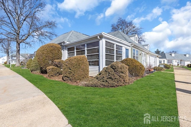 view of home's exterior with a residential view, a sunroom, and a lawn