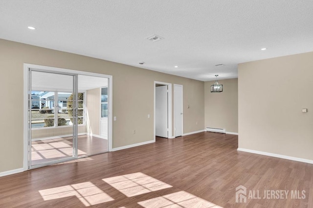 spare room with baseboards, wood finished floors, an inviting chandelier, baseboard heating, and a textured ceiling