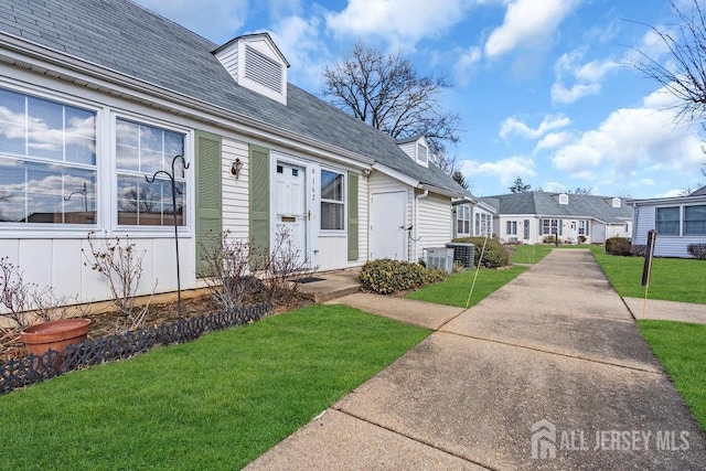 exterior space with central air condition unit, a shingled roof, and a lawn